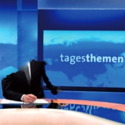 Ein Mann in einem Anzug steht vor einem Fernseher.