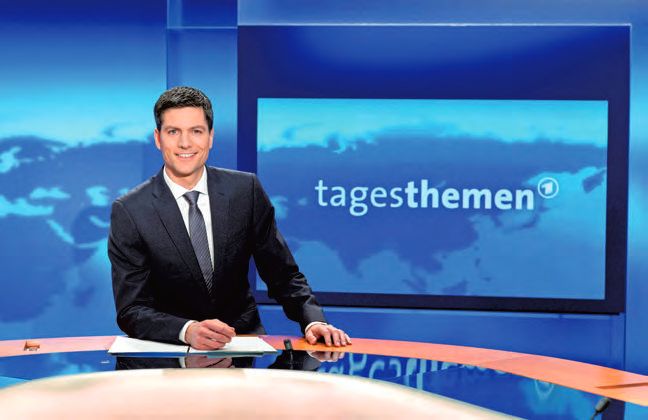 Ein Mann in Anzug und Krawatte sitzt an einem Schreibtisch.