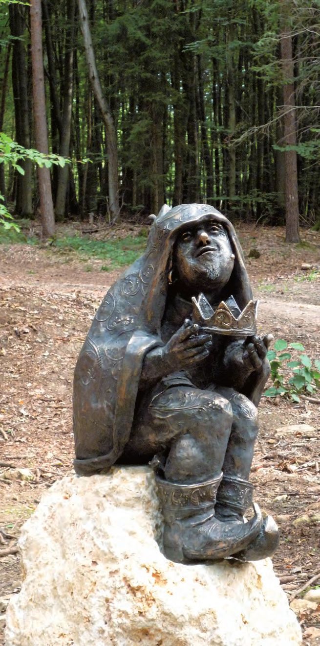 Eine Statue eines Mannes, der auf einem Felsen im Wald sitzt.