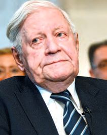 Ein Mann in Anzug und Krawatte mit anderen Männern hinter sich.
