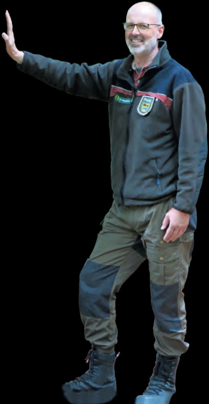 Ein Mann in Jacke und Hose steht mit ausgestrecktem Arm.
