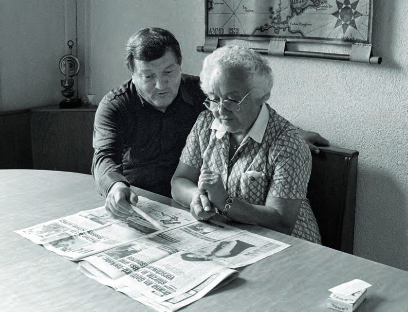 Ein Mann und eine Frau sitzen an einem Tisch und schauen sich eine Zeitung an.