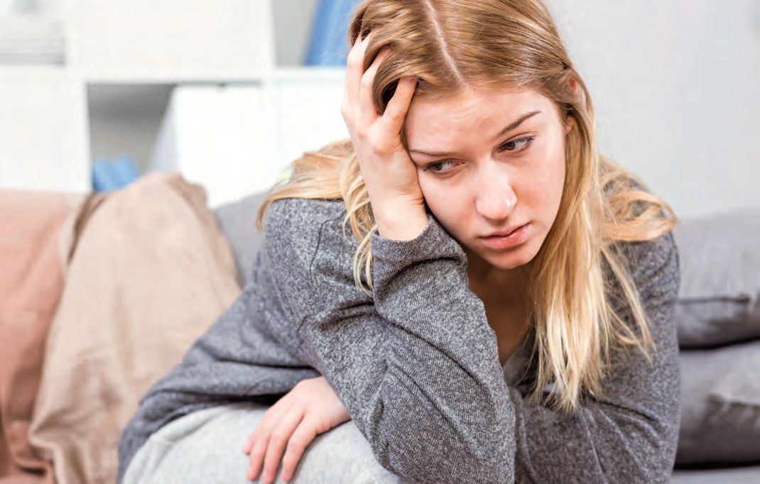 Eine Frau, die auf einer Couch sitzt und den Kopf hält.