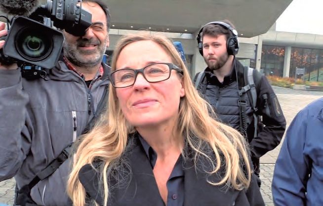 Eine Frau mit Brillen, die vor zwei Männern mit Kopfhörer steht.