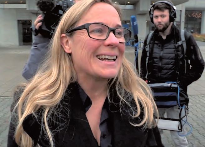 Eine Frau mit Brillen lächelt vor einem Mann mit Kopfhörer.