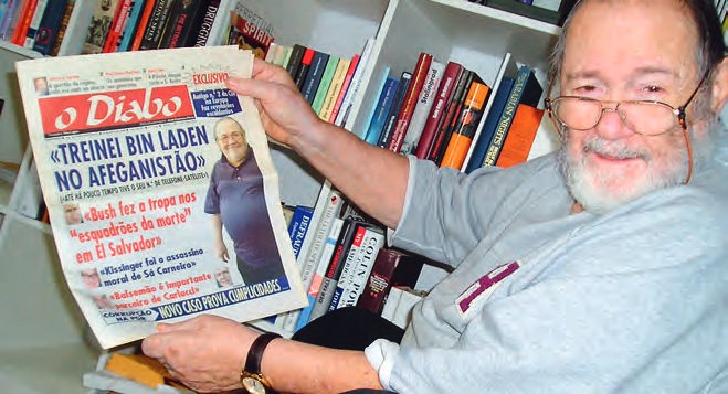 Ein Mann, der eine Zeitung vor einem Bücherregal hält.